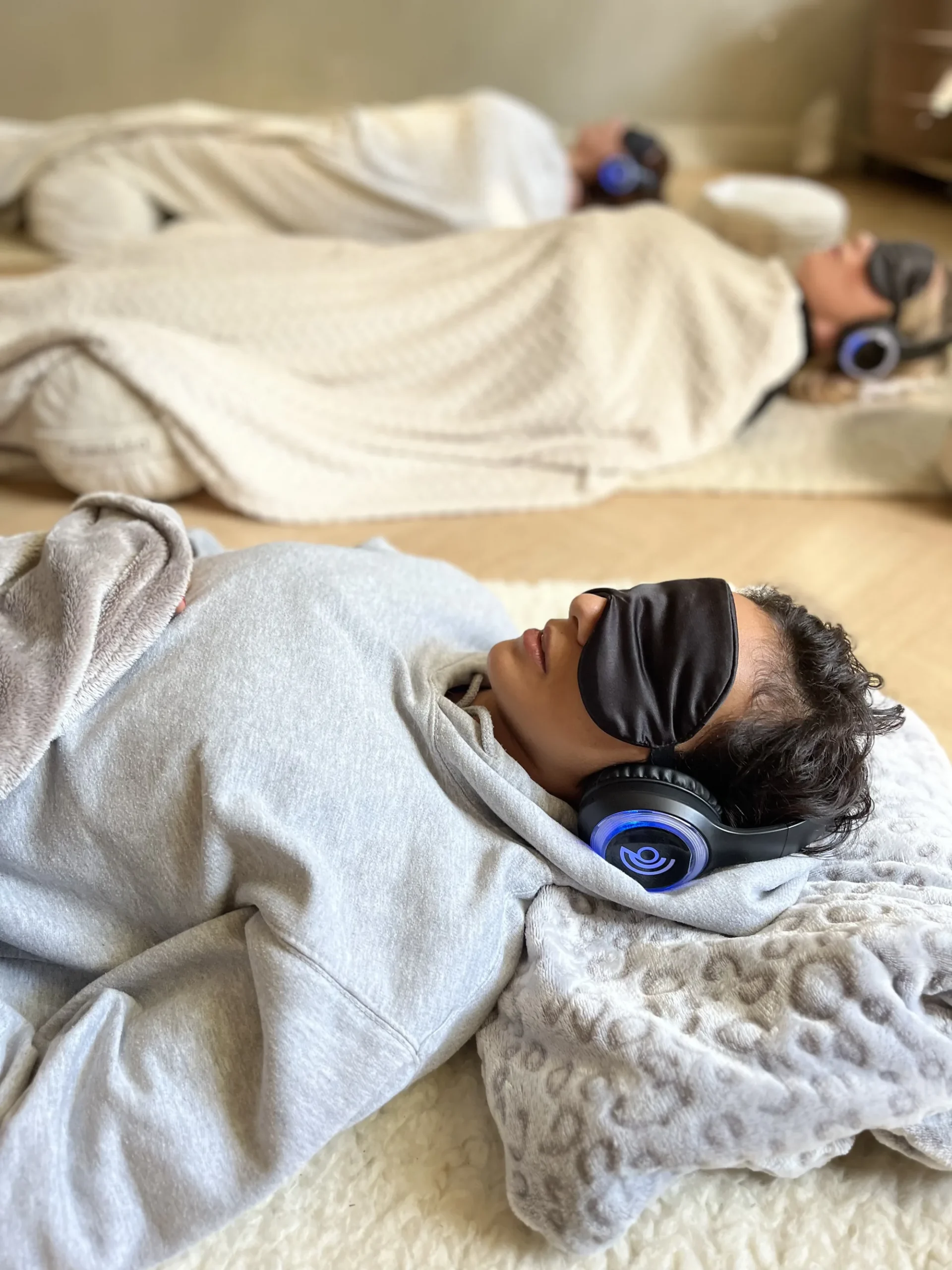 Participants lying on mats in a candlelit 9D breathwork session, wearing eye masks and blue-glowing headphones – the immersive experience of guided breathwork