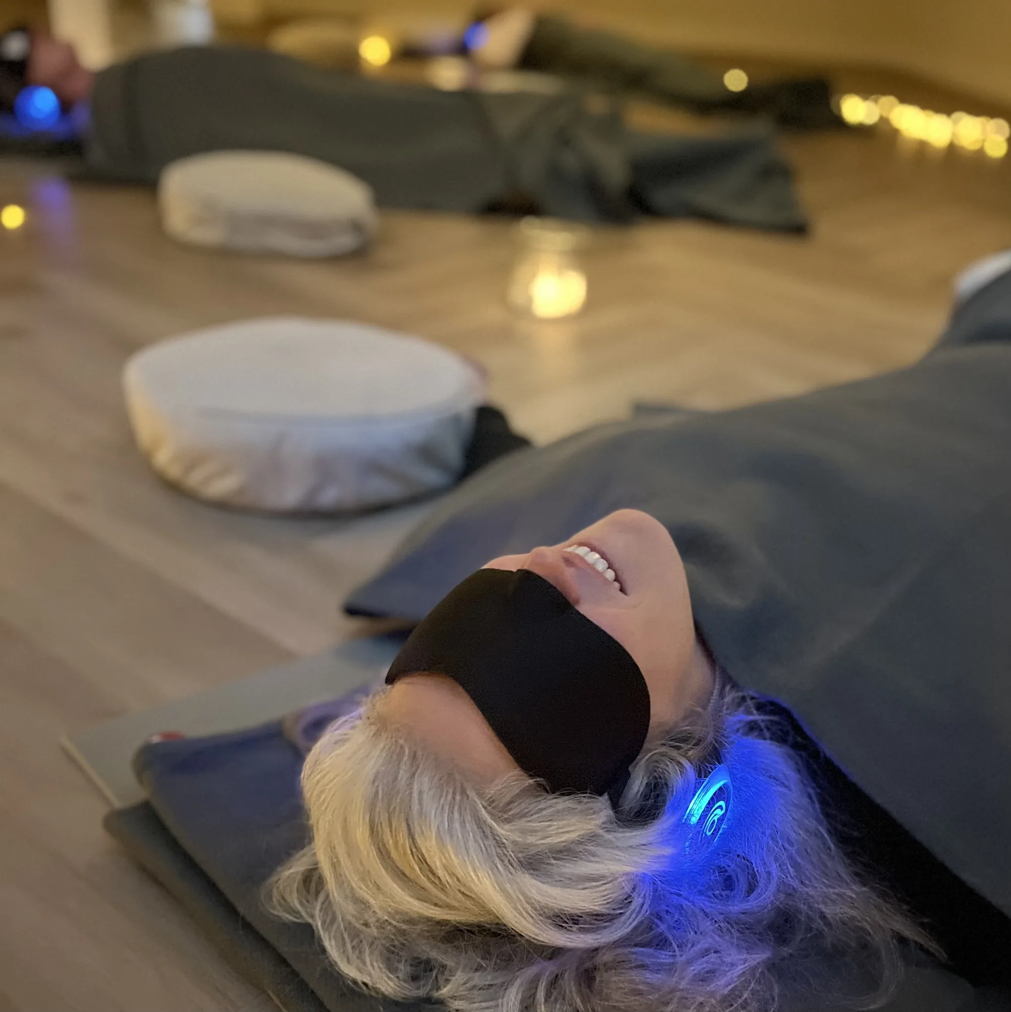 Two people lying wrapped in blankets on the floor with eye masks and 9D breathwork headphones, fully surrendered in a group session at The Reconnected Land
