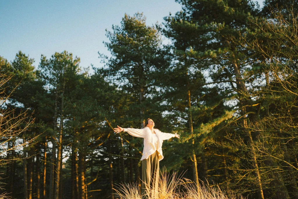 Dany Fenton with arms outstretched on a sandy dune surrounded by pine trees, symbolising the expansive transformation available through corporate breathwork