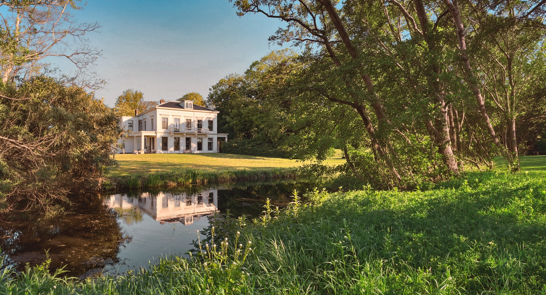 Wide view of the retreat villa and nature grounds of The Reconnected Land seasonal reset day, surrounded by trees and open sky