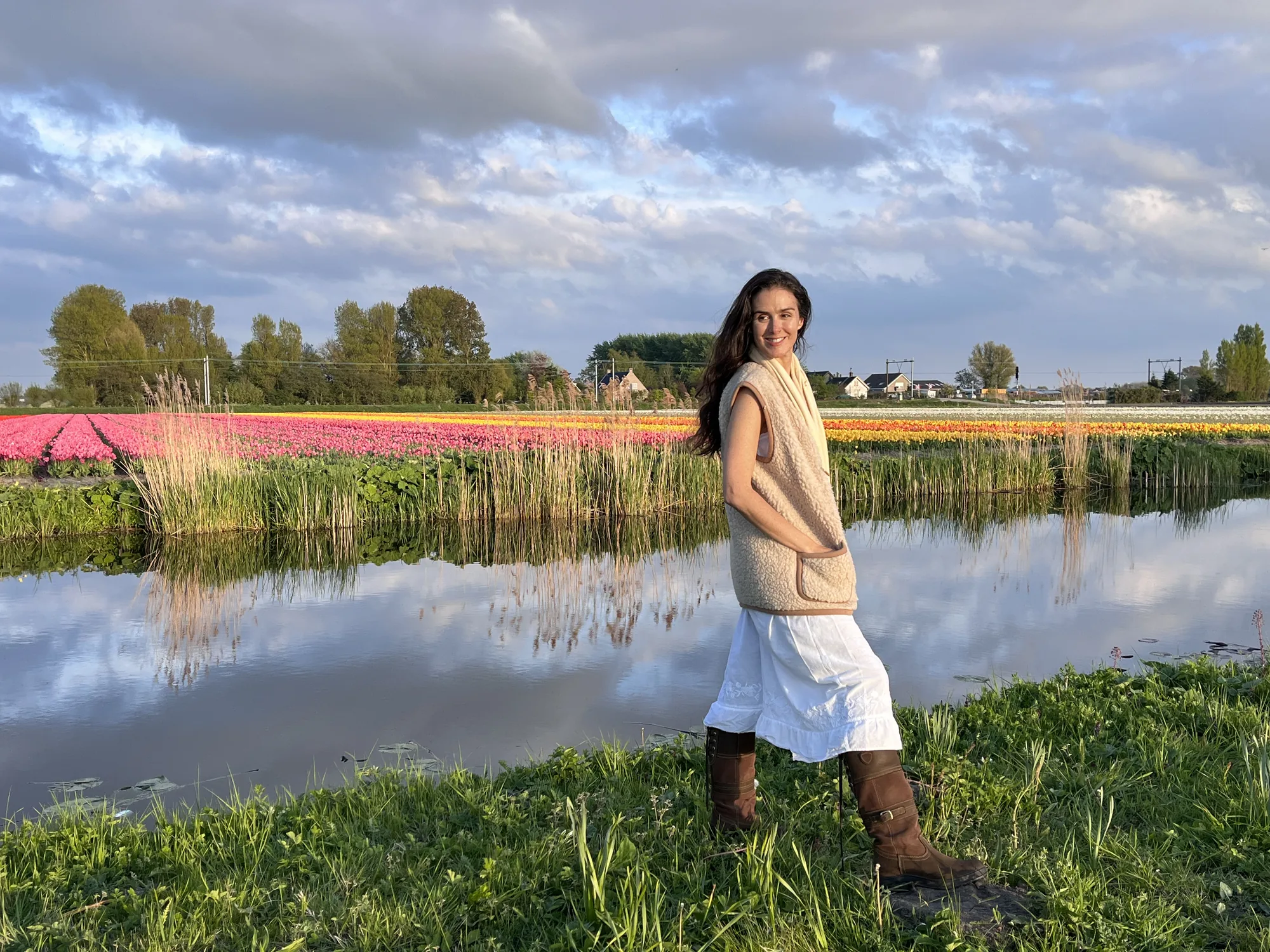 Dany Fenton smiling by a Dutch canal with vibrant tulip fields in full spring bloom behind her, radiating renewal
